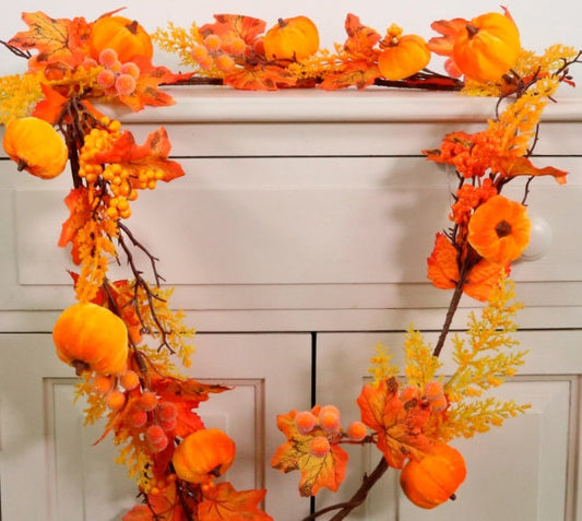 Artificial autumn garland with orange pumpkins and colourful seasonal foliage draped over a cabinet